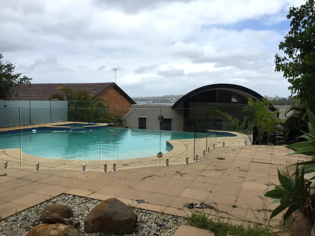 Clear glass pool fencing around a landscaped backyard pool